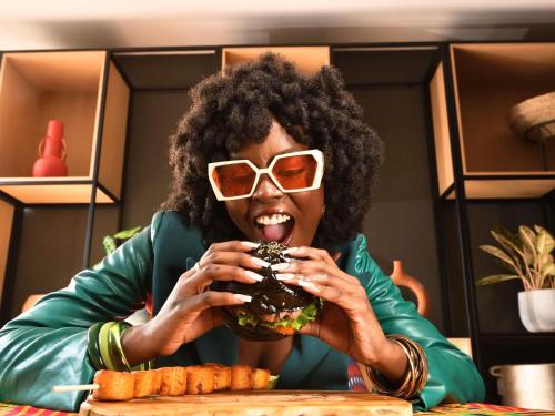 Ibis Styles Abidjan Plateau في أبيدجان: امرأة ترتدي نظارة شمسية وتأكل همبرغر