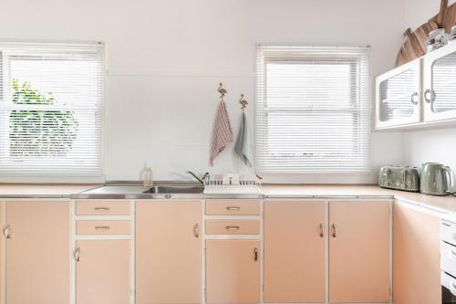 a kitchen with white cabinets and a sink and two windows at Kaimana in Gold Coast