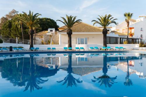 a swimming pool with palm trees and blue chairs at Resort Apartment Cabanas de Tavira in Tavira