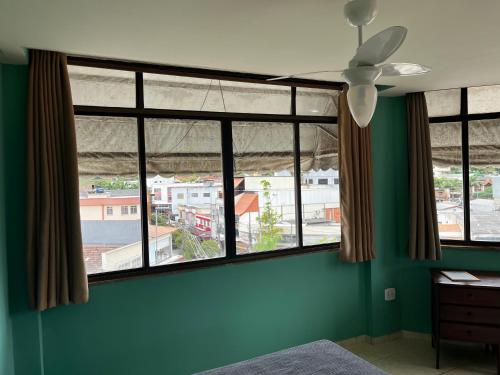 a bedroom with large windows with a view of a city at Kitnet Aurora in Miguel Pereira