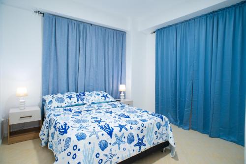 a bedroom with blue curtains and a bed with blue and white sheets at Amplio, cómodo y cerca Del Mar in Porlamar