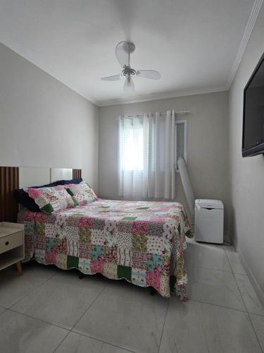 a bedroom with a bed with a comforter and a window at Apto Novo no Canto do Forte PG in Praia Grande
