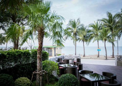 a patio with tables and palm trees and the beach at Kalm Bangsaen Hotel in Bangsaen