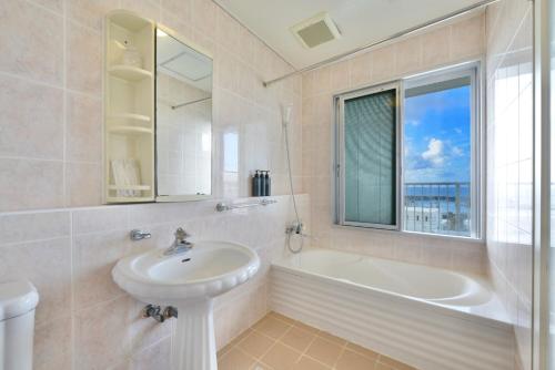 a bathroom with a sink and a bath tub and a window at Sea Side TOYA in Yomitan