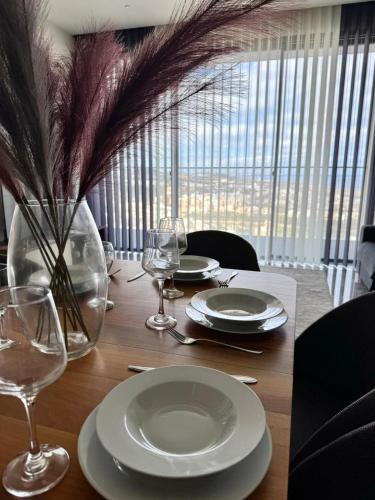 a wooden table with plates and wine glasses on it at Sea view Mercury Tower, Rooftop infinity Pool in St. Julianʼs