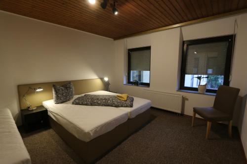 a bedroom with a bed and a chair and two windows at Nadines Ferienwohnung in Krefeld