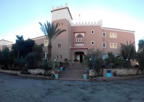 a large pink building with stairs and palm trees at Hotel Les Amandiers in Tafraoute