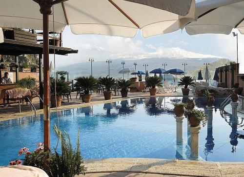 a large swimming pool with plants and an umbrella at Hotel Villa Sonia in Taormina
