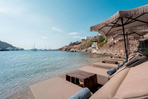 a row of beach chairs with umbrellas and the water at Kivotos Mykonos - Preferred Hotels & Resorts in Ornos