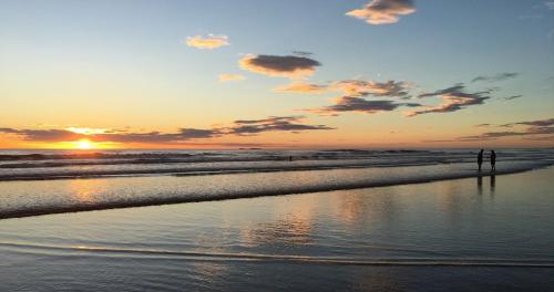 a person standing on the beach at sunset at El Reinas by Sugar's Monkey in Playa Grande