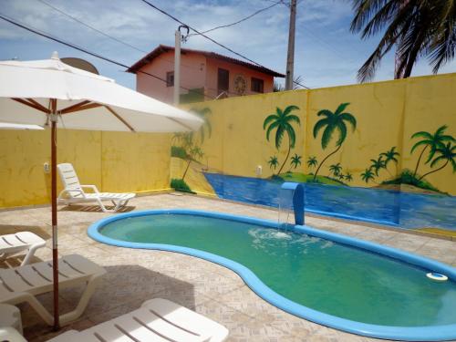 a pool with chairs and an umbrella next to a yellow wall at Pousada Galinhos in Galinhos