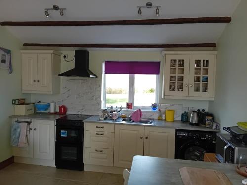 a kitchen with white cabinets and a sink and a window at An Tigín, Gortadoo in Dingle