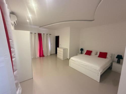 a white bedroom with a white bed and red pillows at House Lima in Lobito