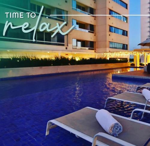 a pool with two lounge chairs next to a building at América Executive Apart Hotel Campos - LAMAG in Campos dos Goytacazes