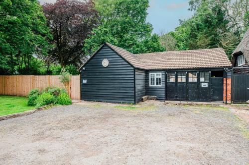 a small black house with a fence and a yard at New Forest Cottage with Hot Tub, Fireplace and Private Garden in Cadnam