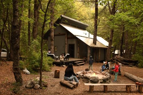 a group of people standing around a cabin in the woods at Curahuapi Refugio de Montaña in Las Trancas