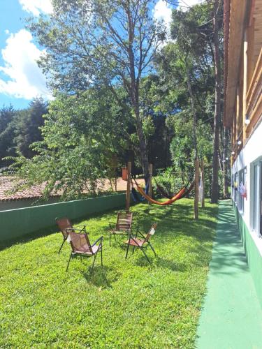 two chairs and a hammock in the grass next to a building at Recanto Ursa Maior in Monte Verde
