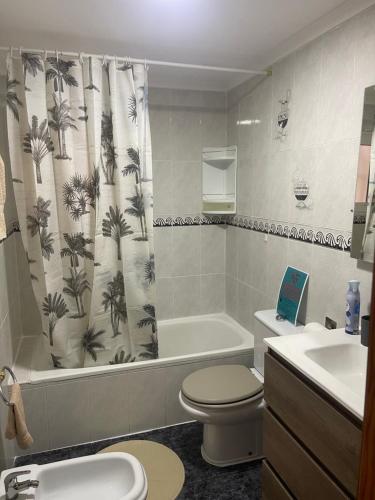 a bathroom with a toilet and a shower curtain with palm trees at Cataleya Apartment in Cullera