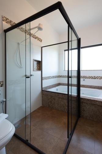 a bathroom with a glass shower and a tub at Pousada Alem das Formas in Carrancas