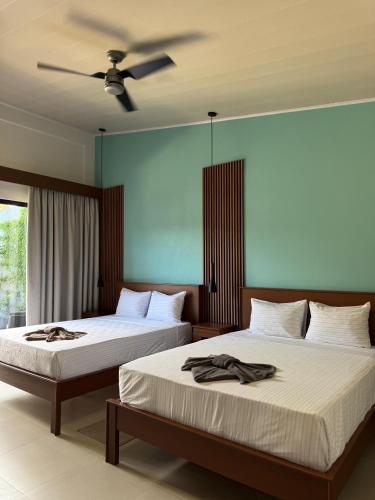 two beds in a bedroom with a ceiling fan at El Jardín de Martín in Puerto Jiménez