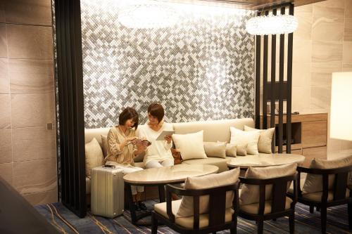 two women sitting on a couch looking at a cell phone at Sotetsu Fresa Inn Ginza-Nanachome in Tokyo