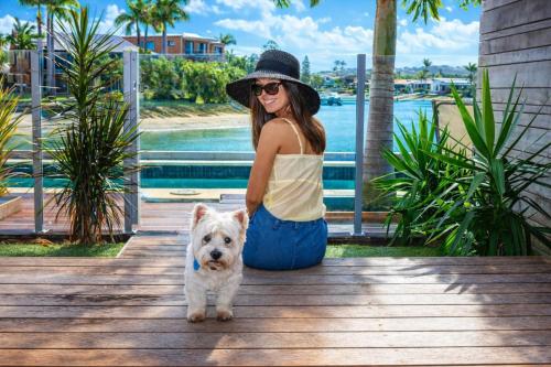 a woman sitting on a dock with a white dog at Saltwater Villas - Pet Friendly Accommodation in Mooloolaba