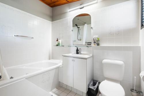 a white bathroom with a tub and a toilet and a sink at Pukeko Guesthouse - Relax in Redcliffe in Redcliffe