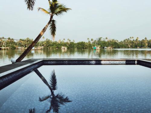 a swimming pool with a palm tree and a body of water at Ambadi's villa -Lake view resort in Pallipuram