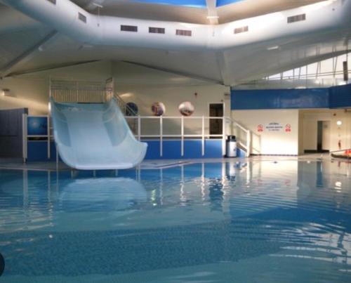 an indoor swimming pool with a slide in the water at Pine Tree Cove - your holiday retreat in Lytchett Minster