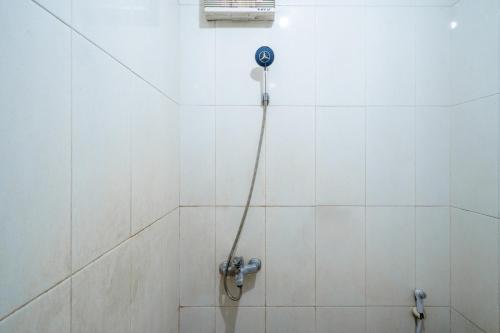 a shower with a hose in a white tiled bathroom at Rehat at Hotel Kurnia Karapitan in Bandung