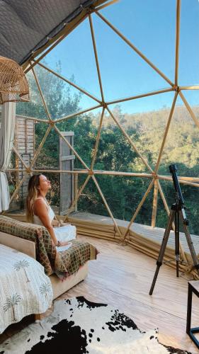 a woman sitting in a chair in a room with a window at Soul Forest GeoDome - Off-grid Nature Escape in Sedgefield