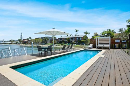 a swimming pool with a deck and a table with an umbrella at Saltwater Villas - Pet Friendly Accommodation in Mooloolaba