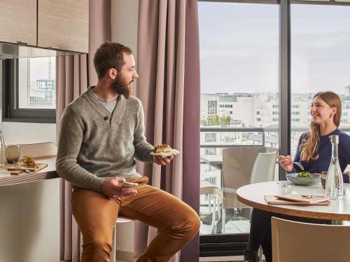 a man and a woman sitting at a table eating food at AppartHotel Mercure Paris Boulogne in Boulogne-Billancourt