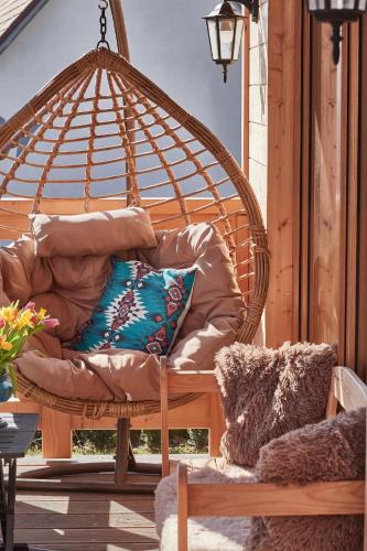 a wicker swing chair with pillows on a porch at Domek Sol Wilcza Zagroda in Kudowa-Zdrój