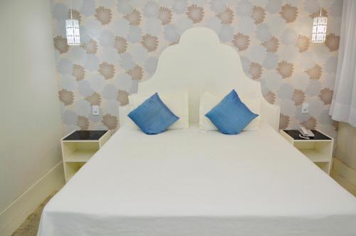 a bedroom with a white bed with blue pillows at Hotel Girassol in Penedo