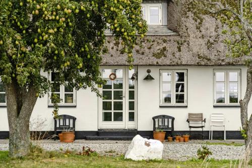 a white house with two chairs and a tree at By The Bay A Thatched House Lies So Beautifully in Nørre Åby