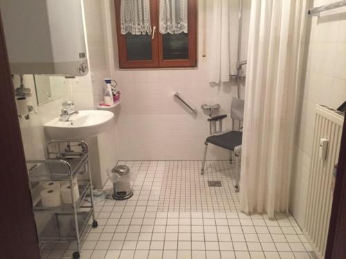 a white tiled bathroom with a sink and a mirror at Barrierefreie Ferienwohnung Bodenseeblick in Unteruhldingen