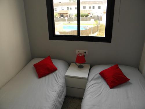 2 camas con almohadas rojas en una habitación con ventana en Apartamento en Jerez de la Frontera en Jerez de la Frontera