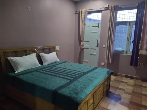 a bedroom with a bed with a green comforter and two windows at The pine view Orchard homestay in Rāmgarh