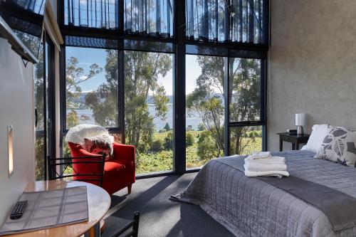 a woman sitting in a red chair in a bedroom with a large window at Tamar River Apartments in Rosevears