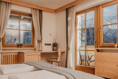 a bedroom with a bed and a desk and windows at Gutonhof in Selva di Val Gardena