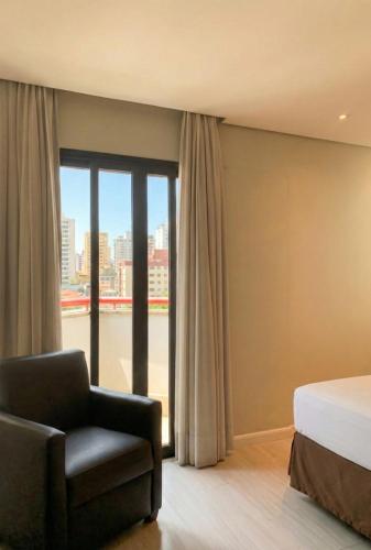 a bedroom with a bed and a chair and a window at Bienal Suítes in São Paulo