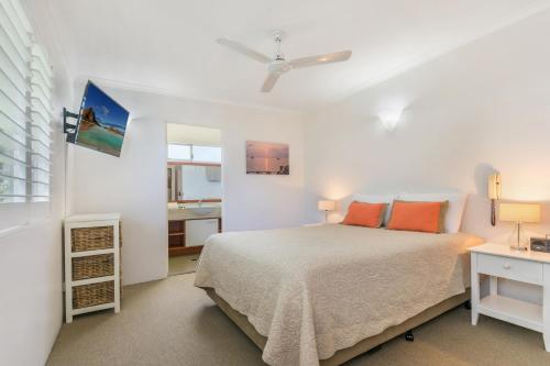a white bedroom with a bed with orange pillows at Bali Hai Apartments Noosa in Noosa Heads