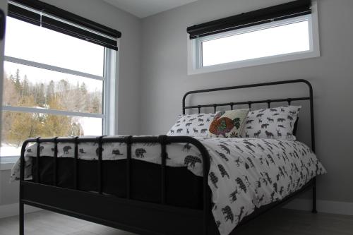 a black bed in a white bedroom with two windows at La Casa TiMoris in Wentworth-Nord