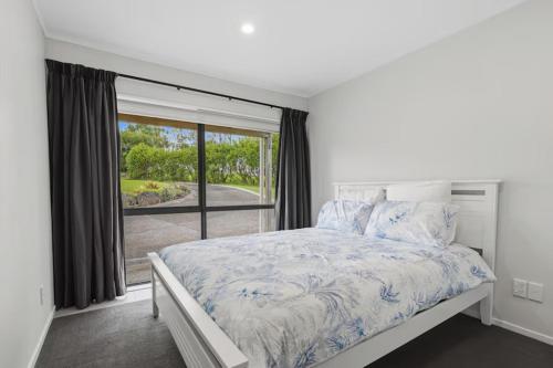 a white bedroom with a bed and a large window at Clay Cottage in Waimauku