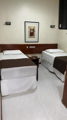 a bedroom with two beds and a picture on the wall at Cheverny Apart Hotel in Belo Horizonte