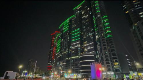 a tall building with green lights on it at night at Beachfront Luxury Family Apartment with Pool, Gym, Jacuzzi - AJMAN Corniche UAE in Ajman