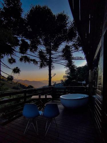 two chairs and a tub on a deck with a view at Chalé Refúgio do Lobo in São Bento do Sapucaí
