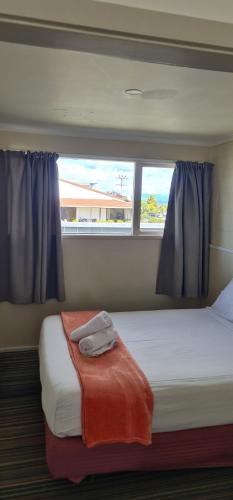 a bedroom with a bed with a blanket and two windows at Kiwi Cove Motel in Taupo