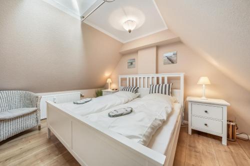 a bedroom with a large white bed and a chair at LH Dünenblick Wohnung 9 in Wenningstedt